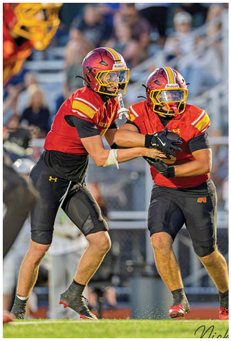 Two football players wearing red and black uniforms. Description generated by AI