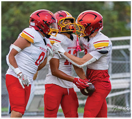Three football players wearing red and white uniforms. Description generated by AI