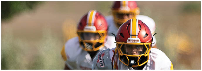A football player in a white jersey and red helmet is bending over to pick up a football. Description generated by AI