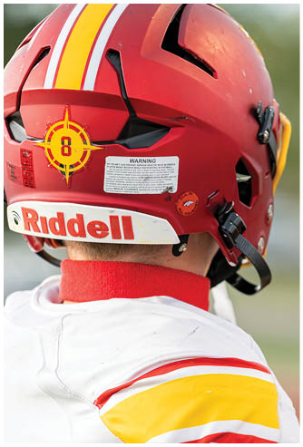 A football player wearing a red and yellow helmet holds a football. Description generated by AI