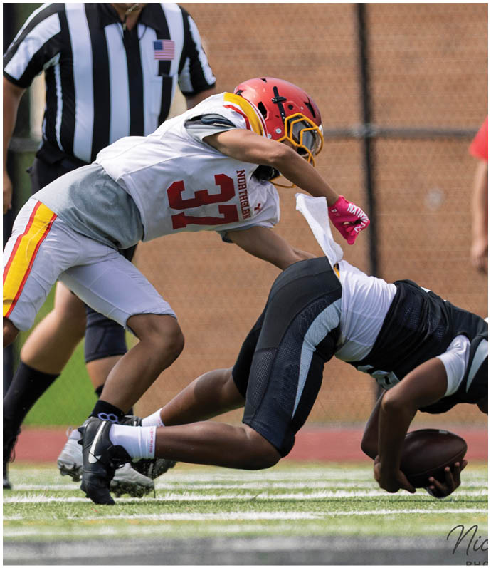 A football player in a black jersey is sliding into a football player in a white jersey. Description generated by AI