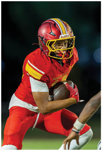 A football player in a red and yellow jersey is running with a football. Description generated by AI