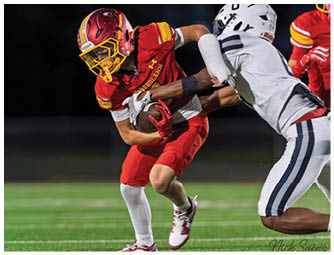 A football player in a red jersey is running with a football. Description generated by AI