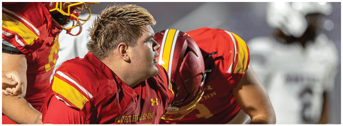 A football player in a red jersey is kneeling down next to another player. Description generated by AI