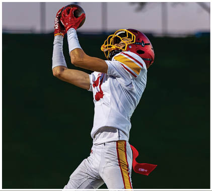 A football player wearing a white jersey with the number 21 on it catching a football. Description generated by AI