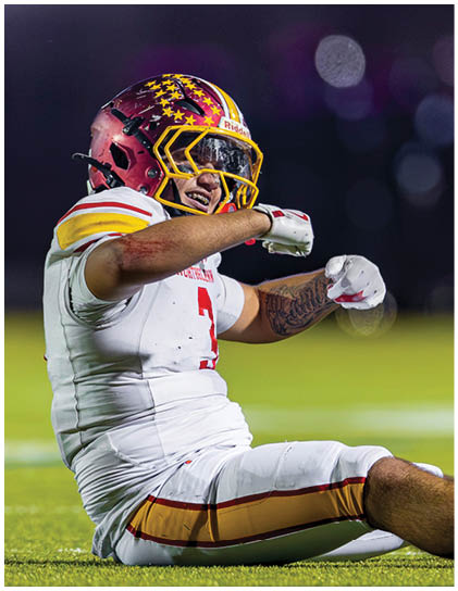 A football player wearing a white and red jersey is sitting on the ground. Description generated by AI