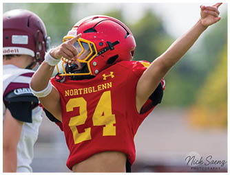 A young boy wearing a red and yellow Northglenn jersey. Description generated by AI