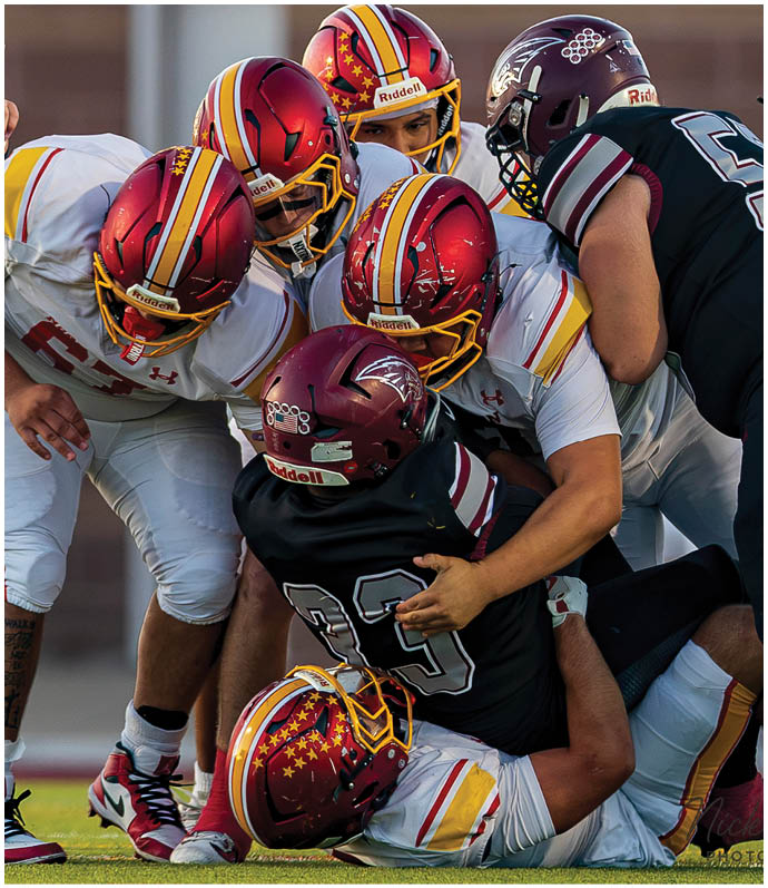 A group of football players in red and white uniforms are tackling a player in a black jersey. Description generated by AI