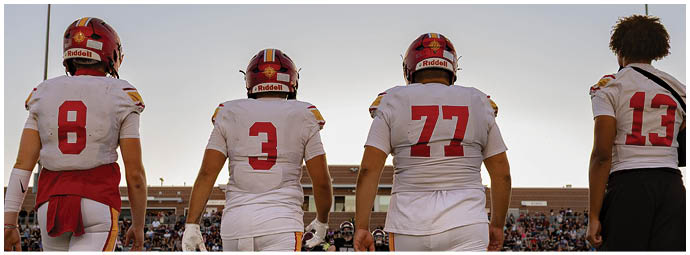 Three football players wearing white uniforms with red numbers on the back. Description generated by AI