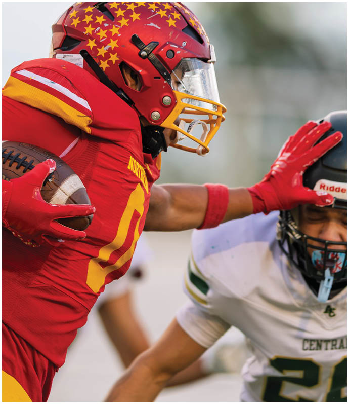 A group of football players in red and white uniforms are tackling a player in a black jersey. Description generated by AI