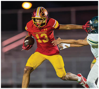 A football player wearing a white jersey with the number 21 on it catching a football. Description generated by AI