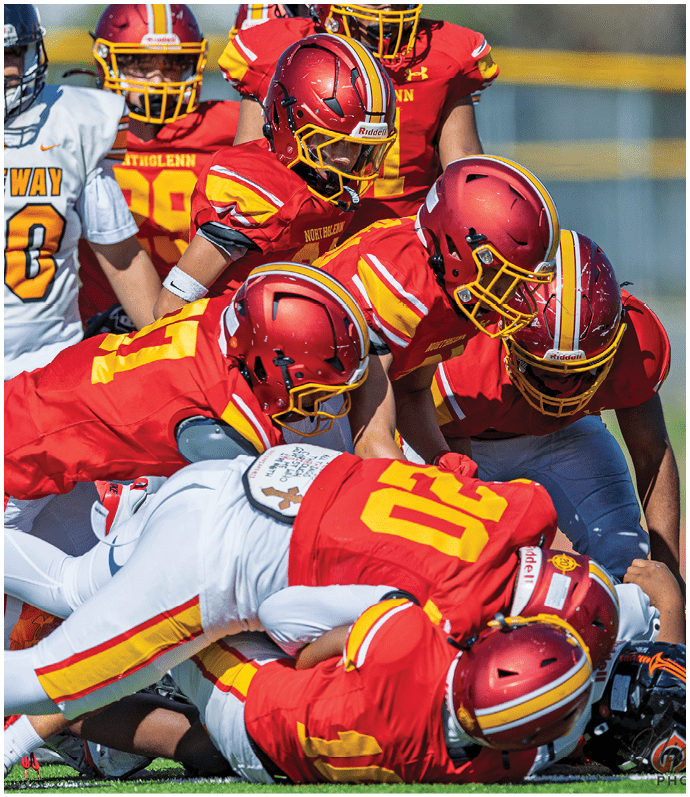 A group of football players in red and white uniforms are tackling a player in a black jersey. Description generated by AI