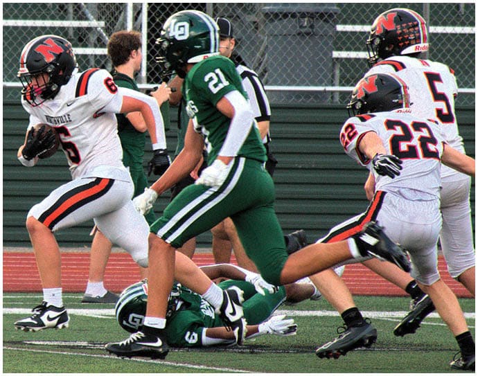 Three football players in blue and white uniforms running on a field. Description generated by AI