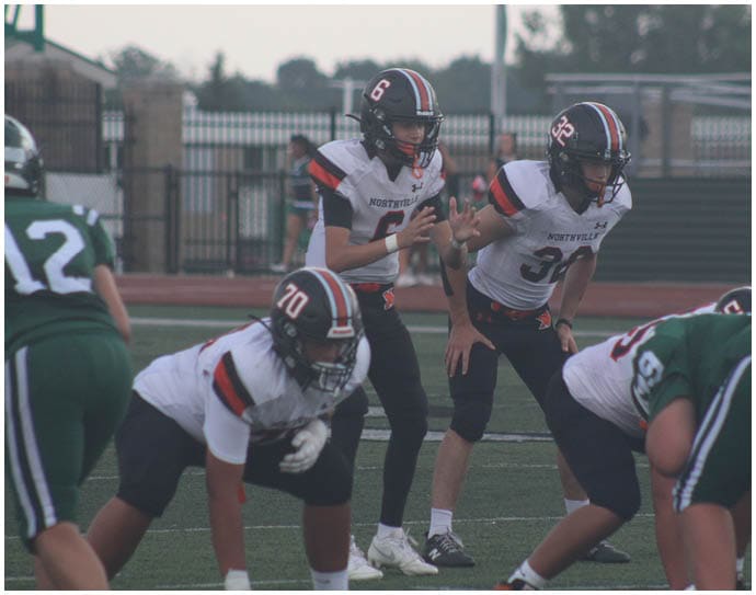 Three football players in blue and white uniforms running on a field. Description generated by AI