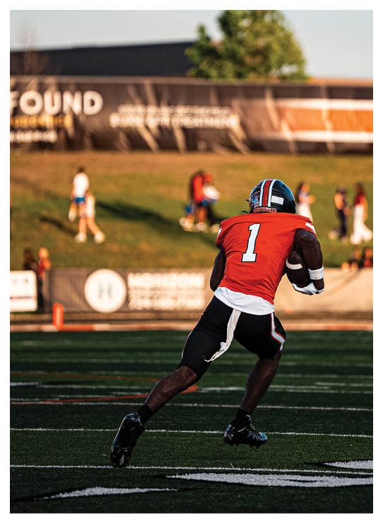A football player wearing a helmet and white uniform is holding his helmet above his head. AI generated content