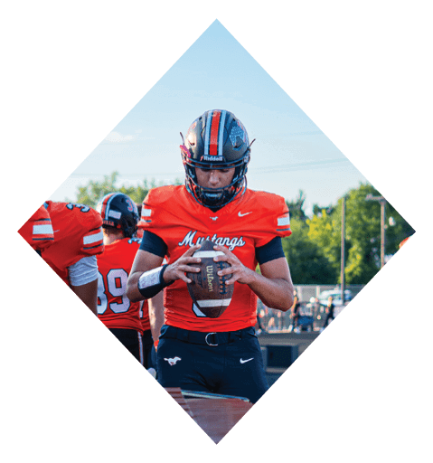 A football player wearing a black jersey with the number 10 sits on the ground with a football helmet on the ground next to him. AI generated content