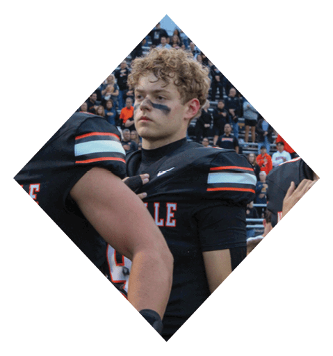 A football player wearing a black jersey with the number 10 sits on the ground with a football helmet on the ground next to him. AI generated content