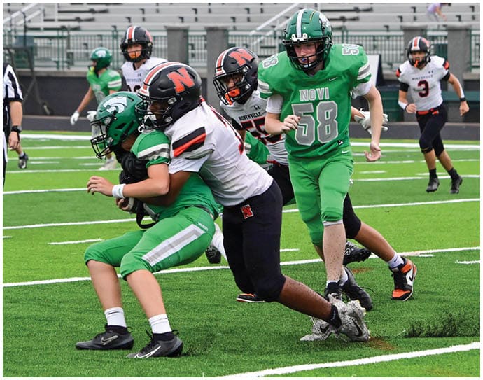 Three football players in blue and white uniforms running on a field. Description generated by AI