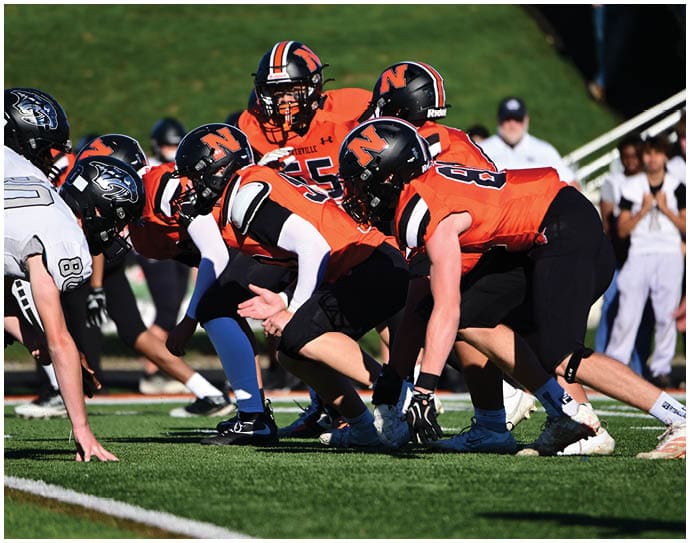Three football players in blue and white uniforms running on a field. Description generated by AI