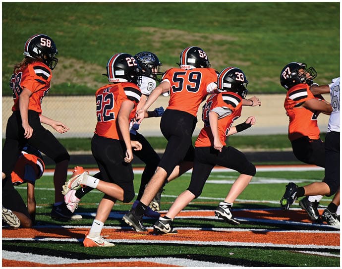 Three football players in blue and white uniforms running on a field. Description generated by AI