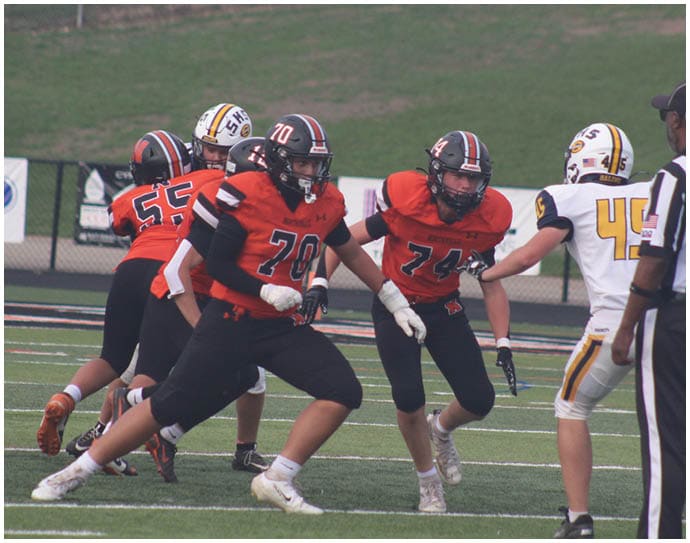 Three football players in blue and white uniforms running on a field. Description generated by AI