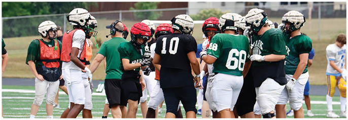 A group of people wearing athletic shoes and socks are standing on a grassy sports field near white yard lines. Description generated by AI