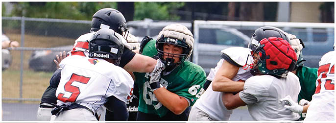 People wearing football uniforms are engaged in a play on a field with a referee and vehicles visible in the background. Description generated by AI