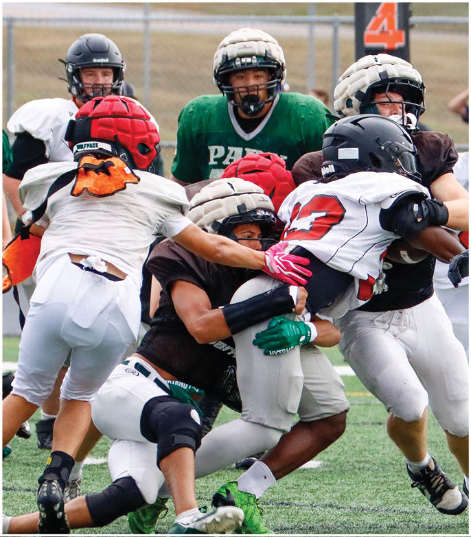 Several people wearing helmets and sports uniforms are engaged in a tackle during an outdoor football game on a grassy field. Description generated by AI