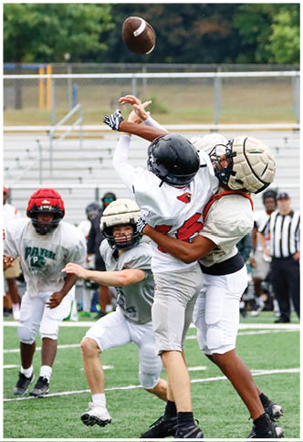 Two people in football gear are reaching up to catch a football in midair on a field. Description generated by AI