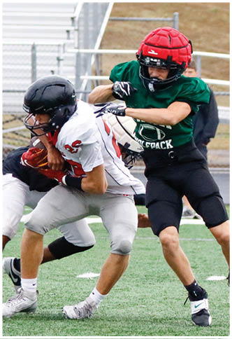 Two people wearing helmets and sports uniforms are engaged in a football tackle on a grassy field. Description generated by AI