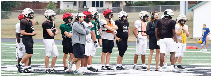 A group of people wearing helmets and sports gear stand on a field, appearing to prepare for or observe a sports activity. Description generated by AI