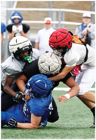 Two people wearing helmets and sports gear are engaged in a tackle during a football game on a grassy field. Description generated by AI