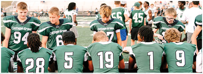 A group of people wearing green sports jerseys with numbers are sitting and standing on a sports field, appearing to be part of a team. Description generated by AI