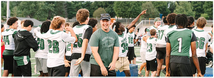 A group of people wearing sports jerseys and casual clothing are gathered outdoors on a field, some smiling and interacting with each other. Description generated by AI