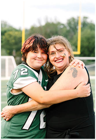 A person wearing a green sports jersey with the number 72 is smiling and hugging another person on a football field. Description generated by AI