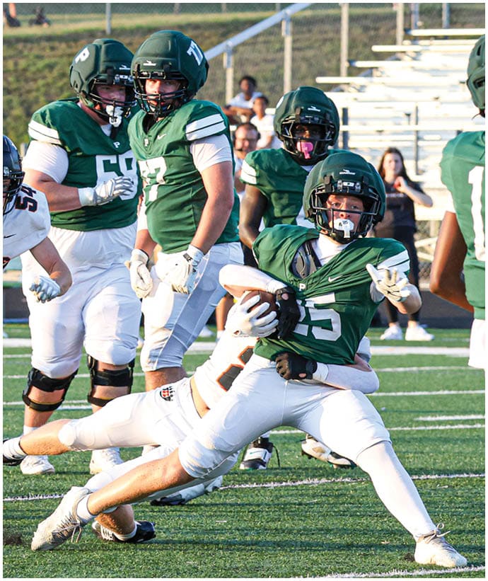 A group of people wearing green and white football uniforms are playing on a field with one person holding the ball while another attempts to tackle them. Description generated by AI