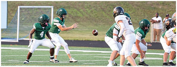 Adults wearing football uniforms are engaged in a play on a field with one person throwing a football while others prepare to catch or block. Description generated by AI
