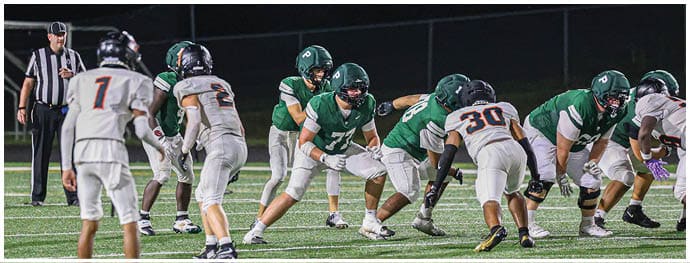 People in football uniforms are lined up on a field at night preparing for a play. Description generated by AI