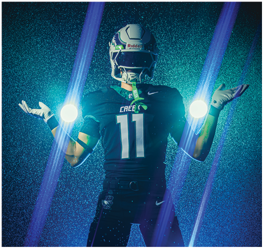 A person wearing a football uniform with the number 11 is standing with arms raised, surrounded by glowing orbs and blue light beams against a dark, textured background. Description generated by AI