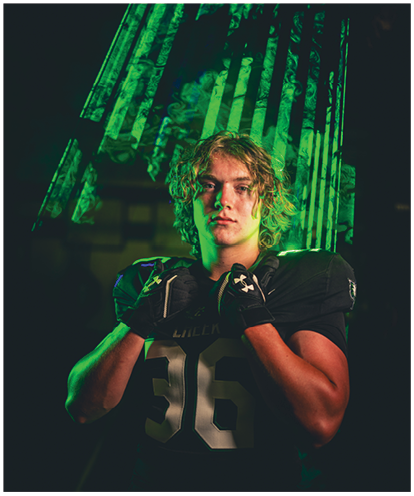 A person with curly hair wearing a black football jersey with the number 36 and black gloves poses confidently against a dark background with green light effects. Description generated by AI