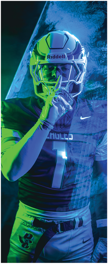 A person wearing a football helmet and uniform is holding a finger to their lips in a shushing gesture against a dark, moody background. Description generated by AI