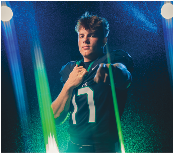 A person wearing a dark sports jersey with the number 17 is posing confidently with one hand on their chest and the other pointing forward against a dark background with colorful light beams. Description generated by AI