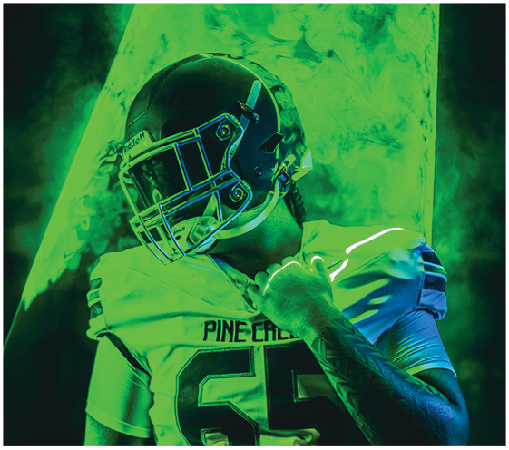 A person wearing a football helmet and uniform is posed against a green smoky background with a bright triangular light behind them. Description generated by AI