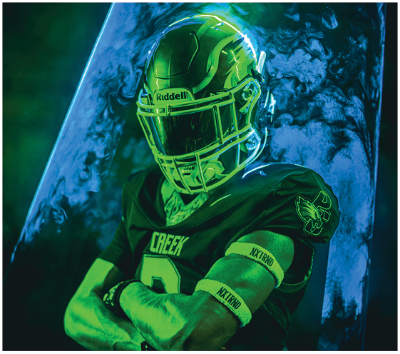 A person wearing a football uniform and gloves poses with hands raised near the face against a green-lit background. Description generated by AI