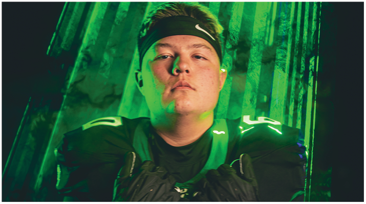 A person wearing a sports jersey and a headband is looking directly at the camera with a serious expression against a green background with vertical stripes. Description generated by AI