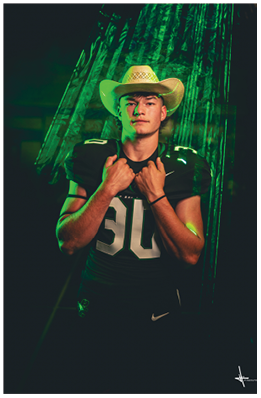 A person wearing a football uniform with the number 50 and a cowboy hat stands confidently against a dark background with green lighting. Description generated by AI