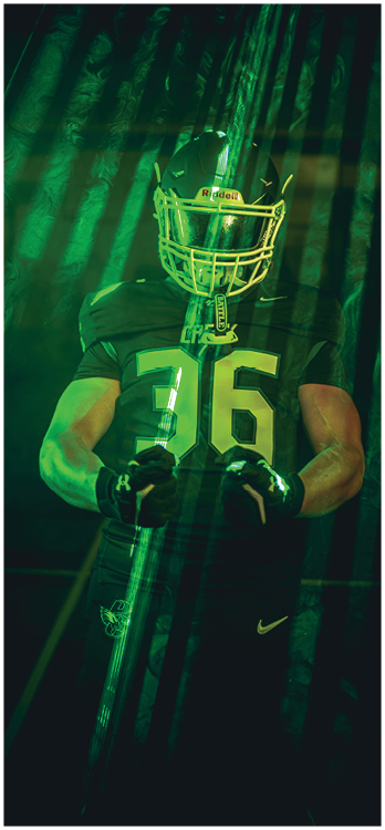 A person wearing a football uniform and helmet stands in front of a green-lit American flag. Description generated by AI