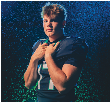 A person with tousled hair wearing a dark sports jersey poses confidently against a dark background with blue light and water droplets creating a dramatic effect. Description generated by AI
