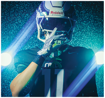 A person wearing a football helmet and uniform with the number 11 is posing with one hand near their face against a backdrop of blue lighting and water droplets. Description generated by AI