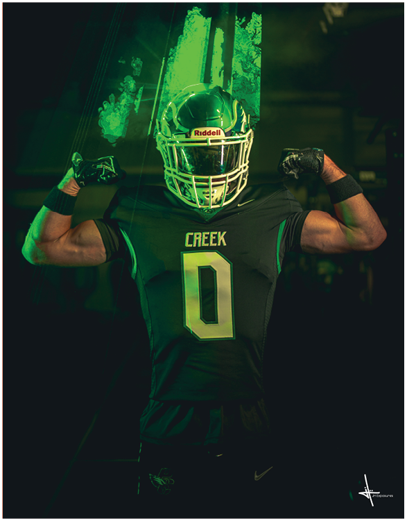 A person wearing a football uniform with the word Creek and number 0 on the jersey is flexing their arm muscles while standing in a dramatic green-lit setting. Description generated by AI